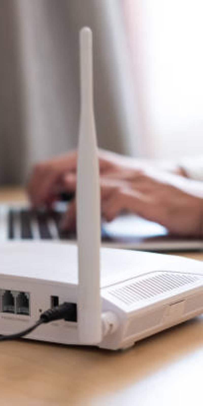 Selective focus at router. Internet router on working table with blurred man connect the cable at the background. Fast and high speed internet connection from fiber line with LAN cable connection.